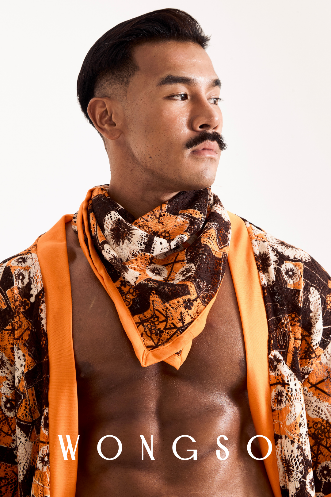 Mid shot of a man wearing a matching sheer orange floral bandana, open relaxed shirt, and beach shorts from WONGSO.