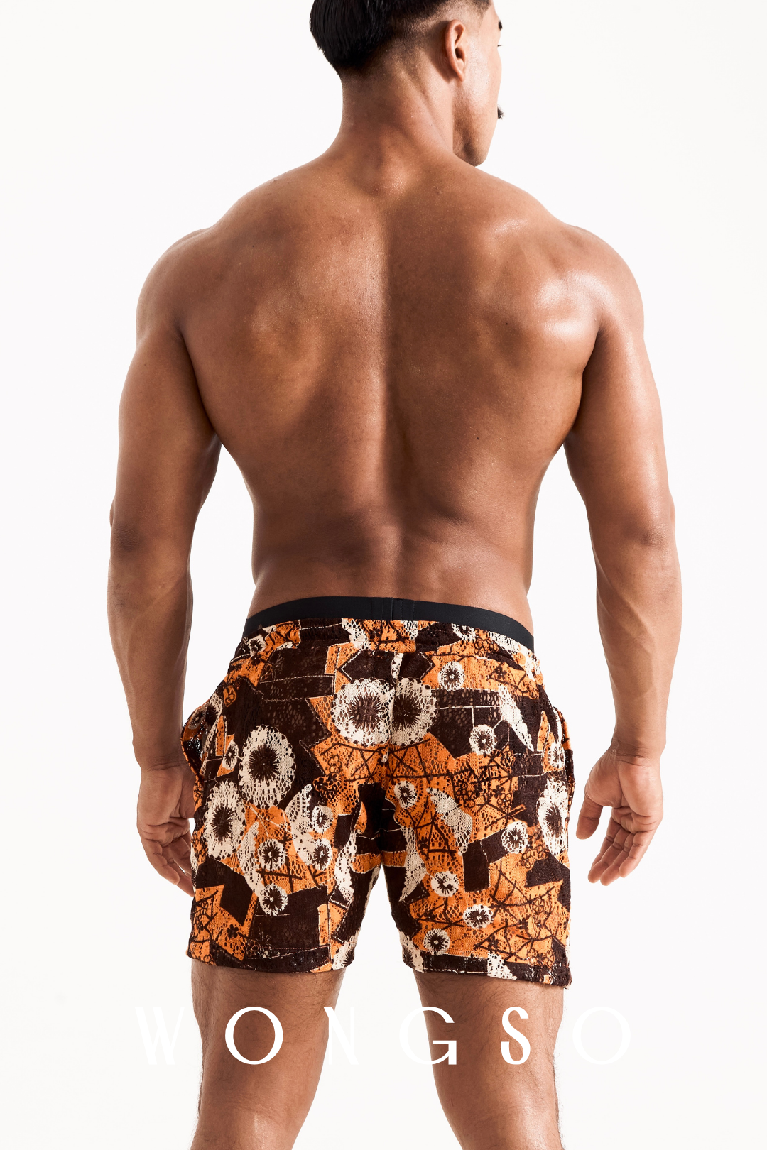 Side profile of a man modeling the sheer orange floral WONGSO beach shorts, highlighting the lightweight, translucent drape.