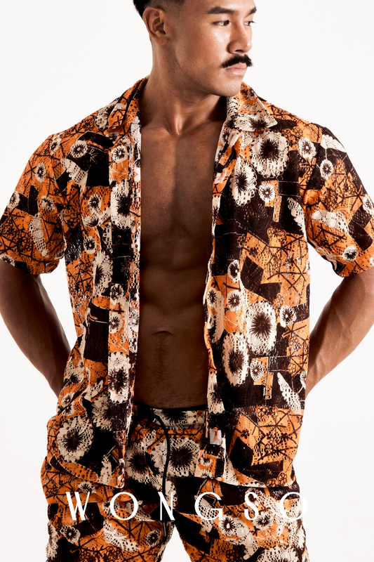 Front mid-shot of a male model wearing the WONGSO sheer sunset orange floral relaxed shirt left unbuttoned over a bare chest.