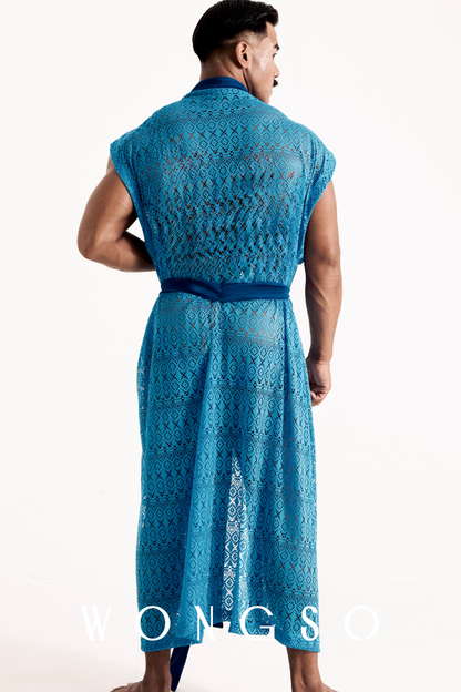 Full body back view of the WONGSO Boheme Sheer Lace Kimono in Bali Blue on a male model. The sweeping, oversized drape of the sheer blue lace showcases subverted Indonesian architectural motifs. Ideal for high-summer festival lounging.