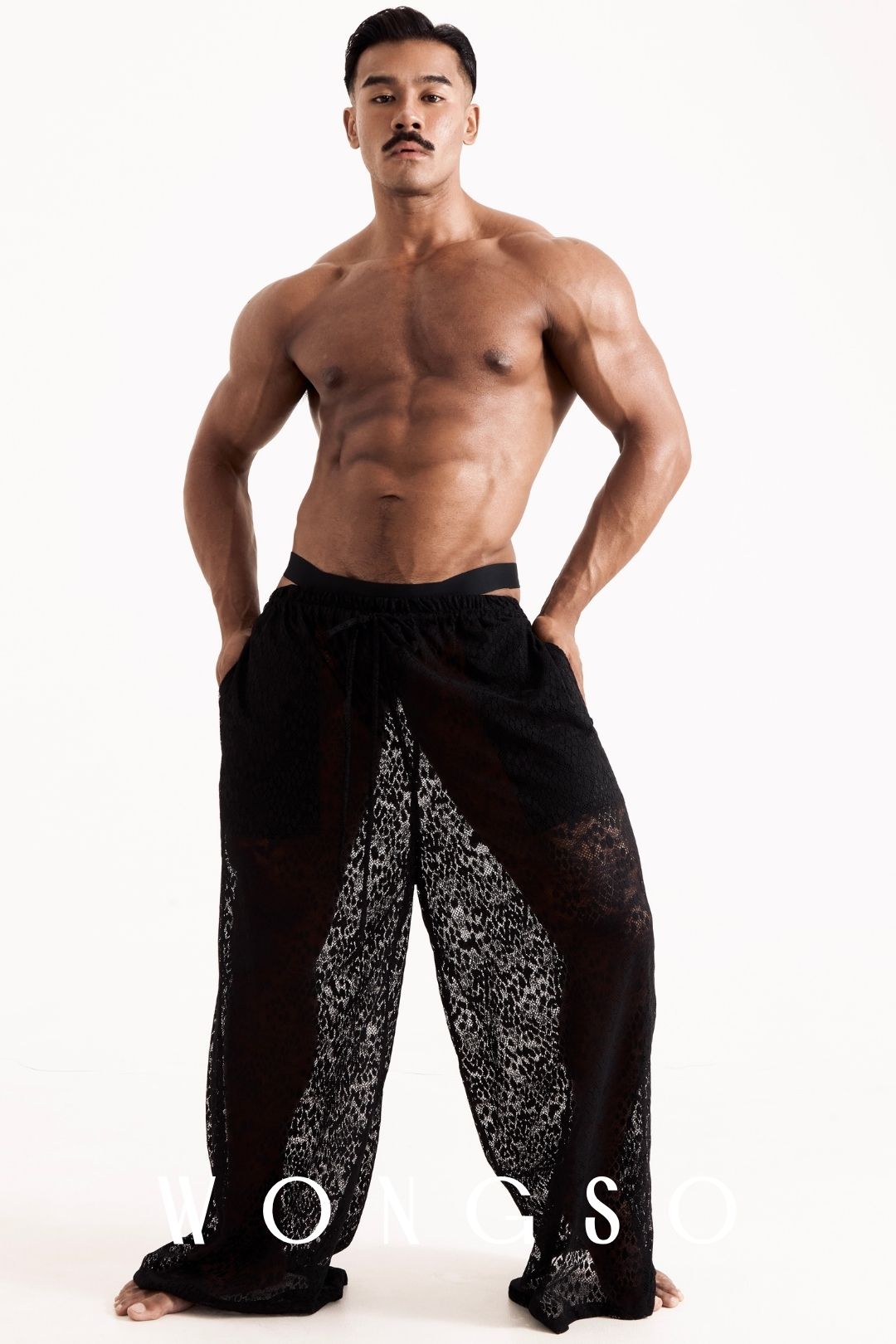 Full body front view of a male model wearing the Libertine Wide Leg Lace Trousers in Leopard Black by WONGSO, billowing sheer silhouette. Men's leopard print festival trousers.