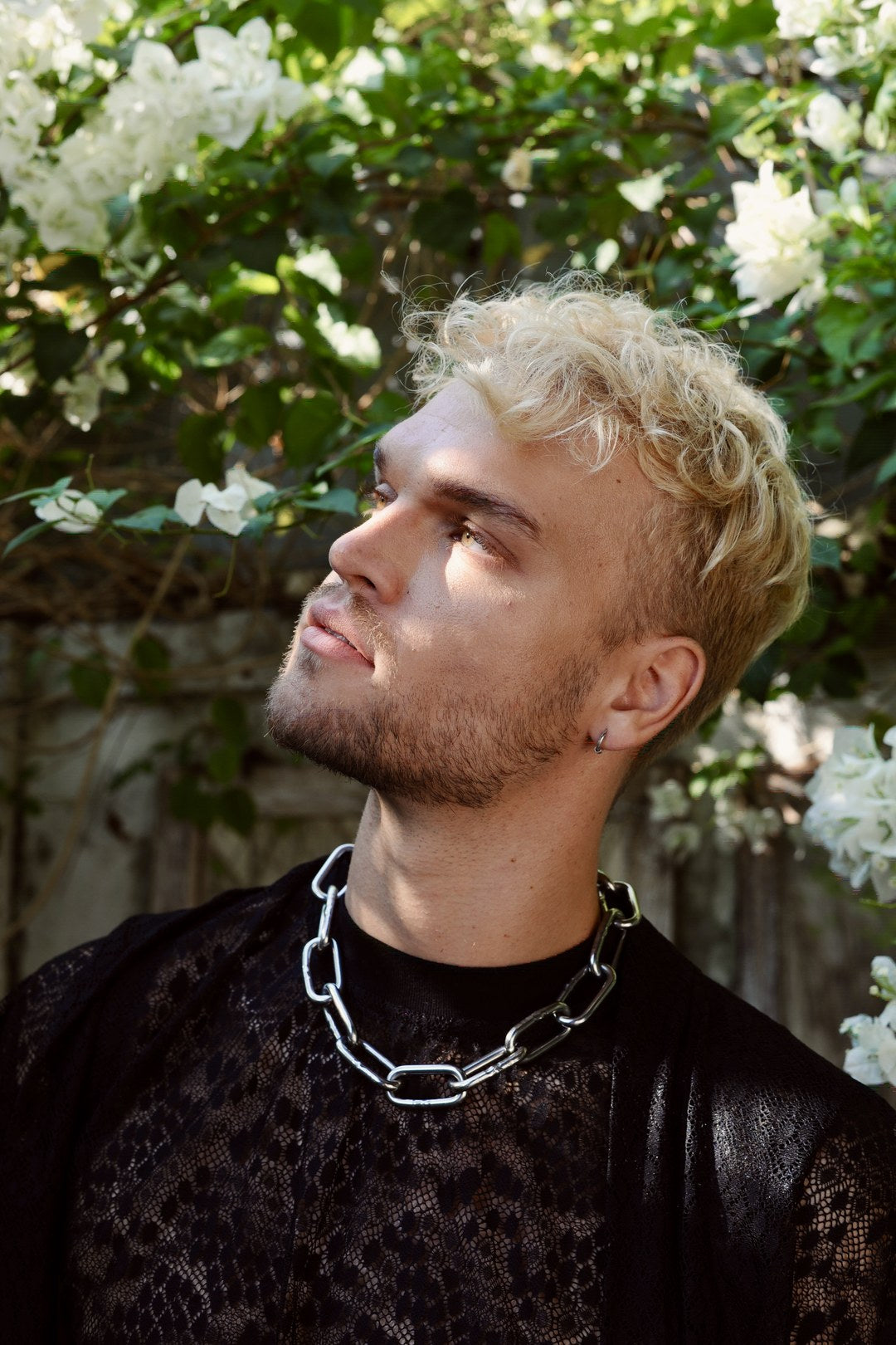 Model wearing the thick steel chain necklace over leopard lace, in a garden