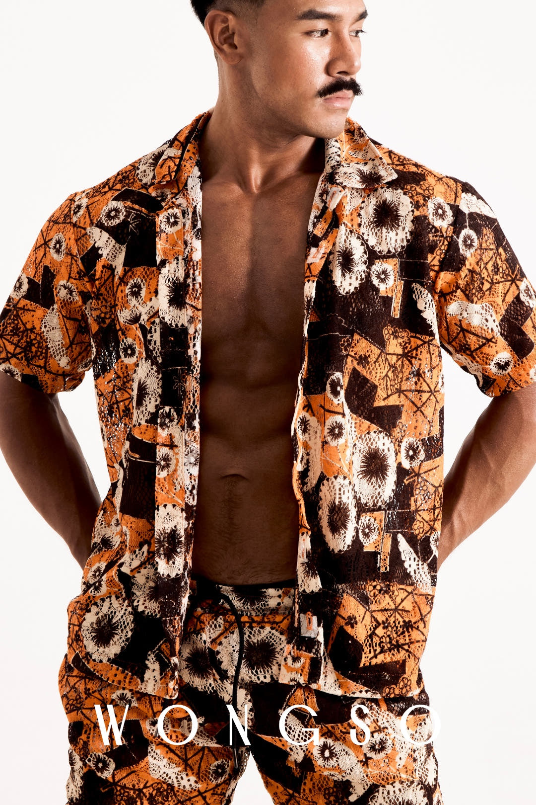 Front mid-shot of a male model wearing the WONGSO sheer sunset orange floral relaxed shirt worn open with camp-collar styling
