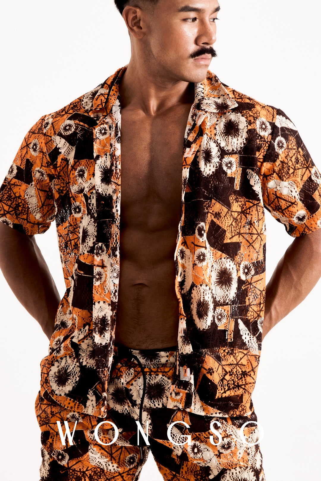 Front mid-shot of a male model wearing the WONGSO sheer sunset orange floral relaxed shirt worn open with camp-collar styling