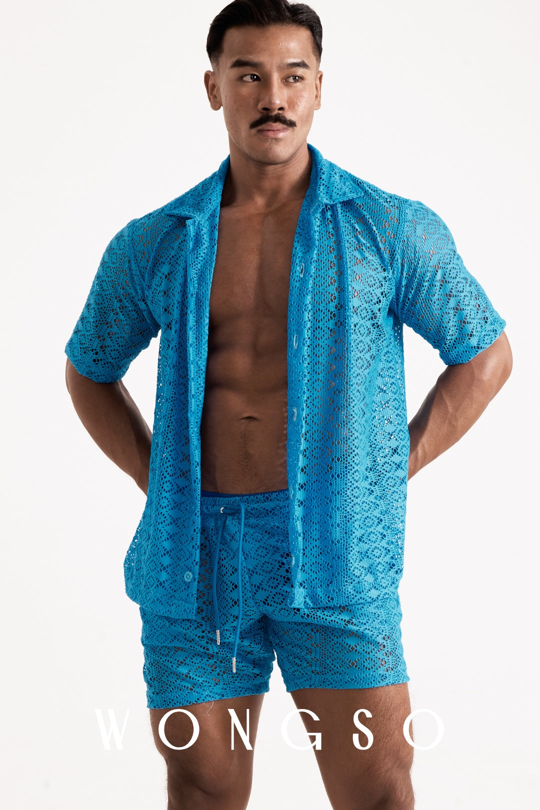 Full body front view of a muscular male model wearing the WONGSO Boheme Sheer Lace Relaxed Shirt in Bali Blue, styled unbuttoned