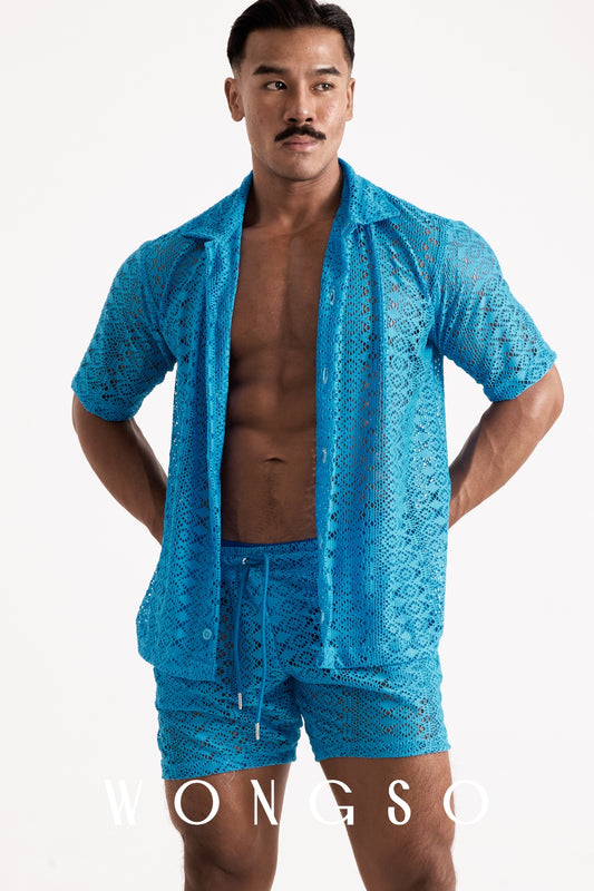 Full body front view of a muscular male model wearing the WONGSO Boheme Sheer Lace Relaxed Shirt in Bali Blue, styled unbuttoned