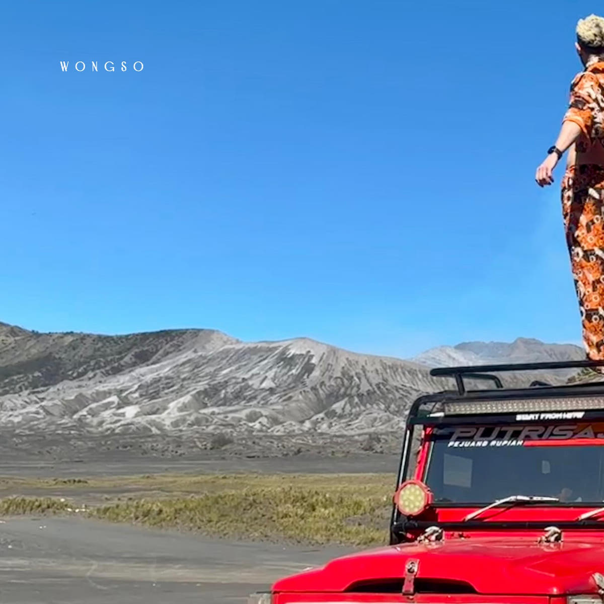 Model in Sunset Orange batik atop a red vintage Land Cruiser with Mount Bromo behind