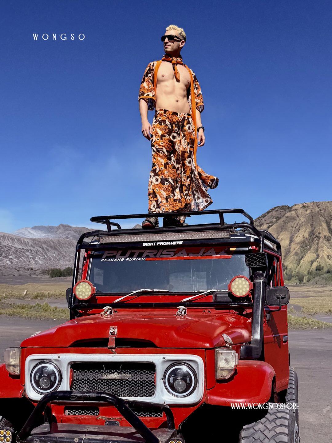 Model in the Sunset Orange batik co-ord standing on a red Land Cruiser, Mount Bromo behind