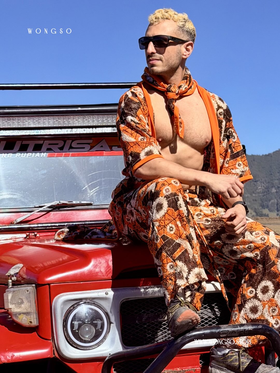 Model in the Sunset Orange batik co-ord seated on a red Land Cruiser