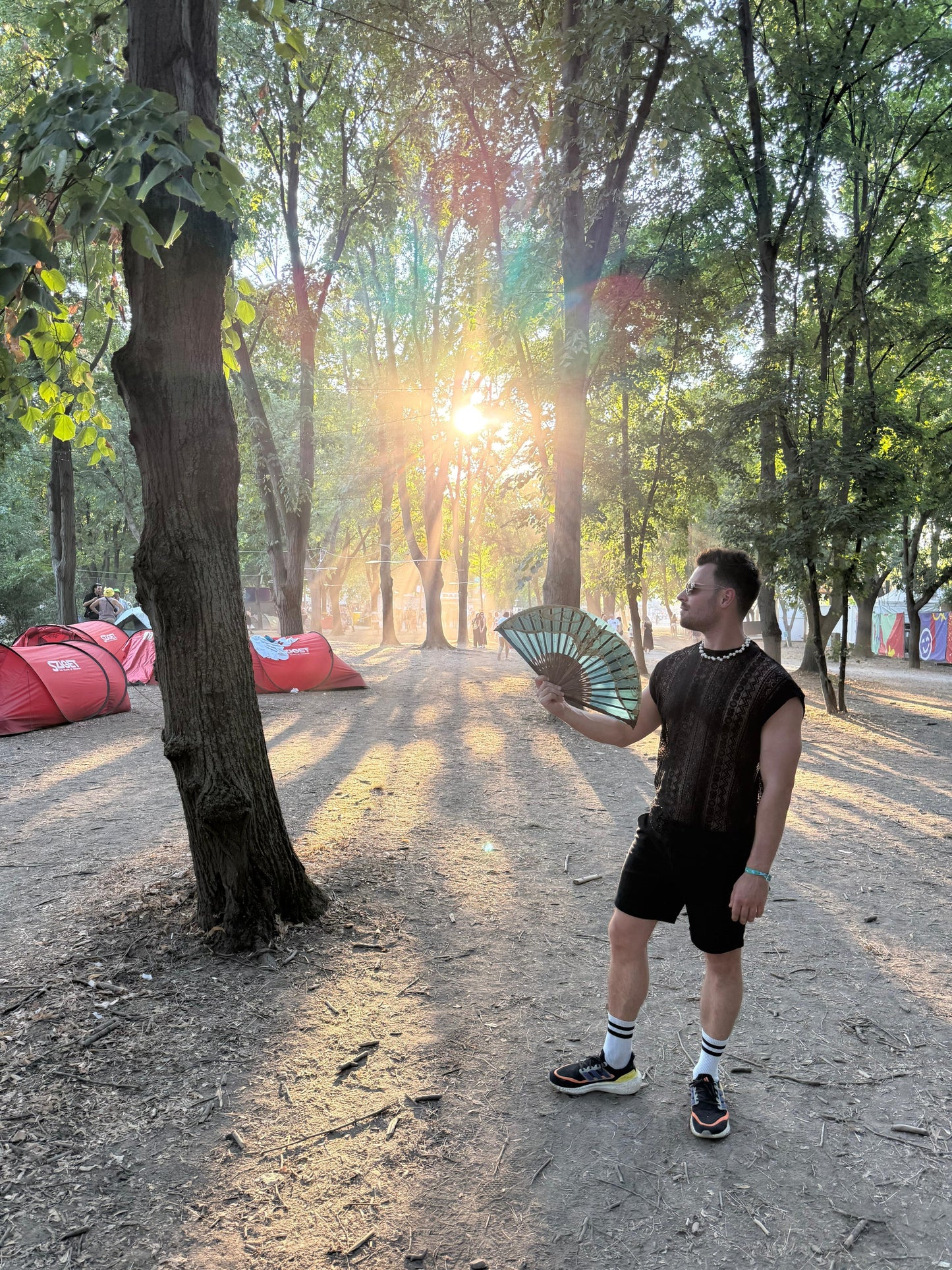 Man wearing the WONGSO Black Lace Festival Shirt with a folding fan at a forest festival campsite at sunset