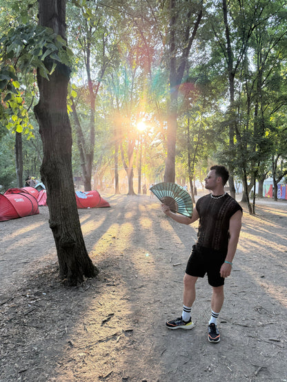 Man wearing the WONGSO Black Lace Festival Shirt with a folding fan at a forest festival campsite at sunset