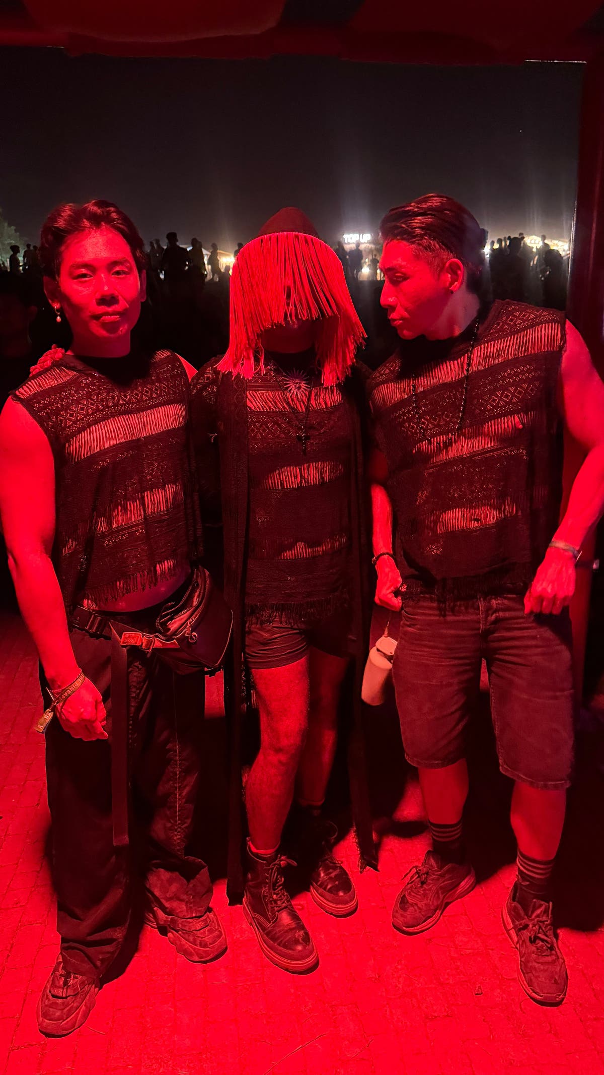 Three friends wearing the WONGSO Fringe Black Lace Festival Tank Top under red stage lighting at a night festival