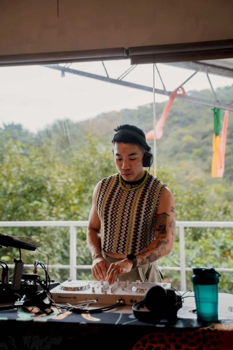 DJ in a zigzag knit sleeveless top from WONGSO playing an outdoor set above the jungle